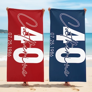 Puede incluir: Dos toallas de playa, una roja y otra azul marino, se muestran sobre un fondo de playa. Cada toalla presenta el nombre "Catherine", el número "40" y la fecha "07.25.1986" en escritura blanca.
