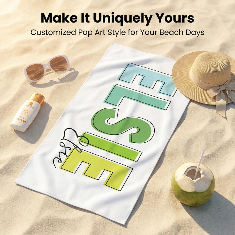 May include: White beach towel with the name "Elise" in a pop art style, featuring blue, green, and yellow lettering. The image includes sunglasses, sunscreen, a straw hat, and a coconut on a sandy surface. Text reads "Make It Uniquely Yours".