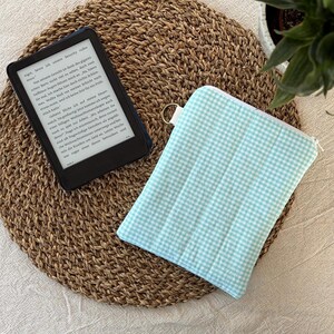 Könnte beinhalten: Ein schwarzer E-Reader mit deutschem Text neben einer rechteckigen, gesteppten Stofftasche mit hellminzgrünem und weißem Vichy-Karo-Muster, versehen mit einem silberfarbenen Reißverschluss und einem kleinen seitlichen Ring zum Aufhängen.