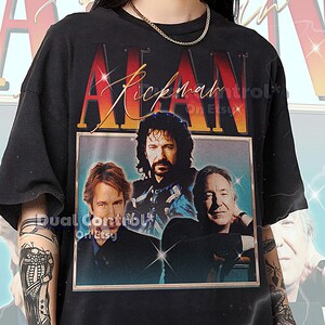 May include: Black t-shirt featuring a graphic of Alan Rickman with the text "Alan Rickman" in a retro style. The shirt has a vintage aesthetic, with a photo of Rickman and the text "Dual Control On Etsy".