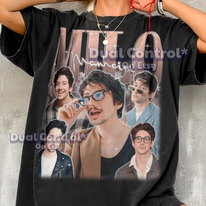 May include: Black oversized t-shirt with a collage of images of a band member. The shirt has the text "MTO" and "Dual Control* Mannheim Etsy" printed on it. The shirt is a dark colour.