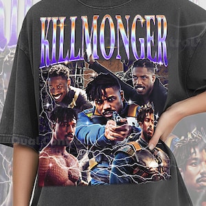 May include: A charcoal gray t-shirt featuring a graphic print with the text KILLMONGER in a metallic purple and orange gradient font. The design includes multiple images of a man with dreadlocks, lightning bolt accents, and a dark background.