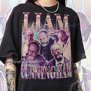 May include: Black unisex t-shirt featuring a graphic of Liam Cunningham with his name in a retro font. The design includes multiple images of the actor. The shirt is a 2XL size and fits true to size.
