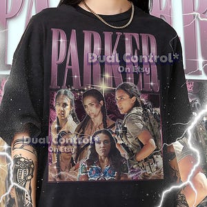 May include: Black unisex t-shirt featuring a graphic of four women with the word "PARKER" in large, purple letters. The shirt includes the text "Dual Control* On Etsy" and sizing information at the bottom.