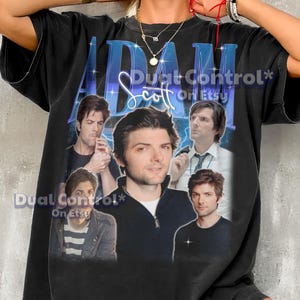 May include: A black short-sleeved t-shirt featuring a large graphic print of actor Adam Scott. The design includes the name ADAM SCOTT in blue lettering and five different photographic portraits of the actor in various outfits and poses.