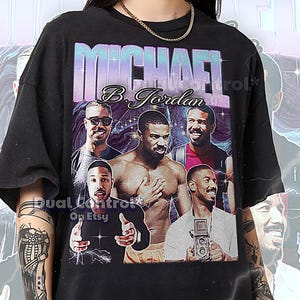 May include: Black unisex t-shirt with a graphic of Michael B. Jordan. The design includes multiple images of the actor with the name "MICHAEL B. Jordan" in a stylized font. The shirt is a 2XL size.