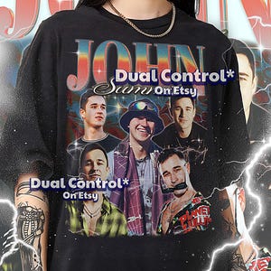 May include: Black unisex t-shirt featuring a graphic design with the text "JOHN" and "Dual Control* Sam On Etsy". The design includes multiple images of people. The shirt also has text at the bottom.