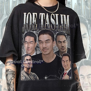 Può includere: T-shirt unisex nero con grafica di Joe Taslim. Il design include più immagini del suo volto e la scritta "JOE TASLIM" in un font metallico. La maglietta ha uno stile vintage.