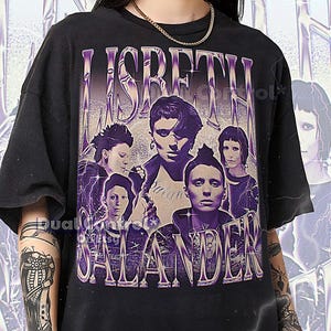 Può includere: T-shirt unisex nero con grafica viola in stile vintage. Il design presenta il testo "LISBETH SALANDER" e ritratti di diverse persone. La maglietta è realizzata in tessuto scuro.
