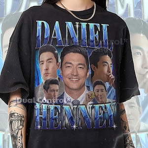 Könnte beinhalten: Schwarzes Unisex-T-Shirt mit einer Grafik von Daniel Henney und seinem Namen in blauem Farbverlauf. Das Design enthält mehrere Bilder des Schauspielers. Das Shirt hat einen Rundhalsausschnitt und kurze Ärmel.