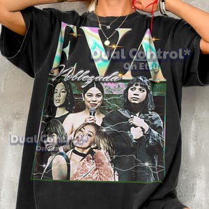 Può includere: T-shirt nero oversize con una grafica in stile vintage di un gruppo di donne e il nome "Noblezada". La maglietta ha un aspetto sbiadito e presenta un design "EVA" colorato.