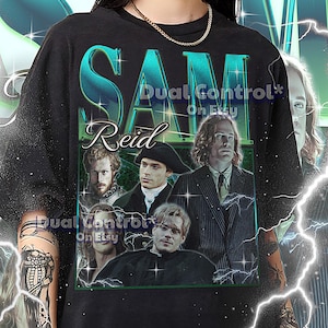 May include: Black unisex t-shirt featuring a graphic of the name "Sam Reid" in teal and white, with a photo collage of actors. The shirt includes the text "Dual Control On Etsy" and sizing information at the bottom.