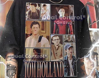 May include: Black t-shirt with a collage of images of Tom Holland, including his role as Spider-Man. The text "Dual Control*" and "TOM HOLLAND" are printed on the shirt.