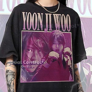 May include: Black unisex t-shirt featuring a graphic of two women with the text "YOON JI WOO" in a purple font. The shirt has a vintage aesthetic. The text "Dual Control* On Etsy" is also visible.