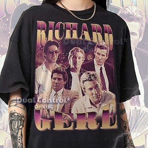 May include: Black unisex t-shirt featuring a graphic of Richard Gere and the text "RICHARD GERE" in a purple and gold retro font. The shirt has a vintage style design with a faded look.