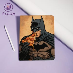 May include: Notebook featuring a comic-style illustration of Batman eating pizza. The artwork depicts Batman in his classic black and gray costume, with a slice of pepperoni pizza in hand. The notebook has a vintage-style background.