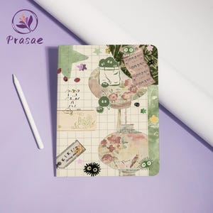 Könnte beinhalten: Ein Notizbuch mit einem Collage-Design mit Cartoon-Charakteren, floralen Elementen und japanischem Text. Das Cover hat ein Rastermuster mit verschiedenen Aufklebern und Illustrationen in Grün-, Rosa- und Beigetönen. Ein weißer Stift liegt daneben.
