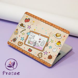 May include: A beige laptop hard shell case featuring a central illustration of an open planner with a white rabbit character, surrounded by colorful icons of strawberries, donuts, honey, stars, and desserts, framed by a brown scalloped border.