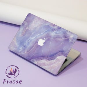 May include: A laptop with a purple and white marble-patterned case. The case features a white Apple logo. The laptop is open, revealing the keyboard and screen. The brand name "Prasae" is visible in the lower left corner.