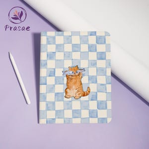 May include: A notebook with a blue and white chequered pattern. The cover features a watercolour illustration of a ginger cat holding two fish. A white stylus and the brand name "Prasae" are also visible.