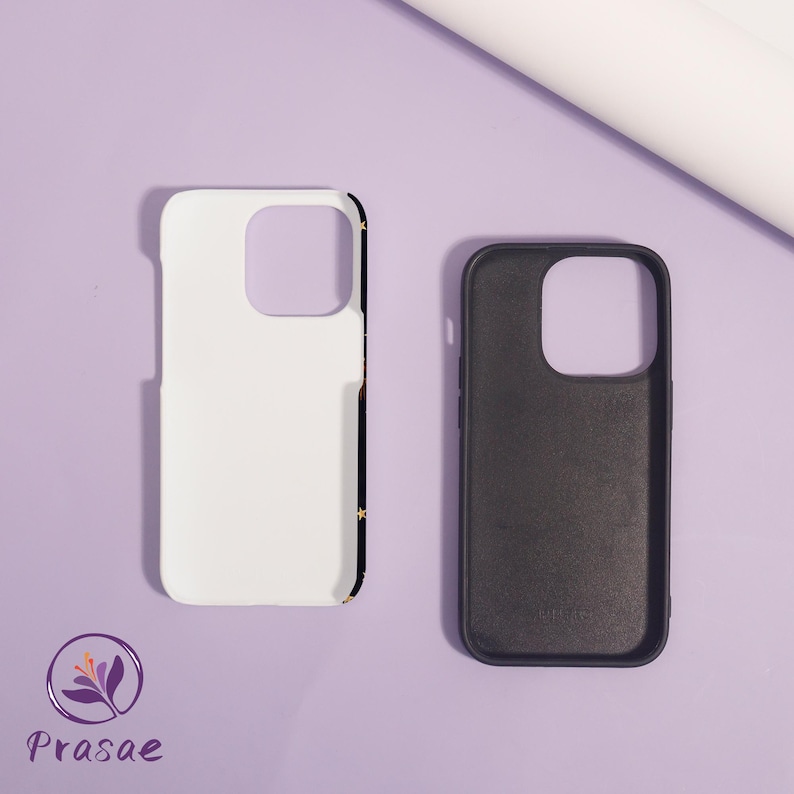 May include: Two phone cases, one white and one black, are shown on a light purple surface. The white case has a black border with gold stars. The black case is open, revealing the interior. The brand logo is visible in the lower left corner.