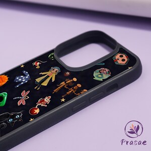 May include: Black phone case with a dark background adorned with colourful cartoon illustrations. The design includes a girl in a yellow coat, a black cat, and other whimsical characters. The case has a black border and a logo in the bottom right corner.