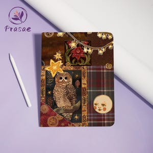 Peut inclure: Un carnet rectangulaire avec une couverture style collage représentant un hibou brun perché sur une branche, entouré d'étoiles, d'un visage de lune, de motifs floraux et de textures écossaises dans des tons marron, vert, rouge et or, avec un stylet blanc.
