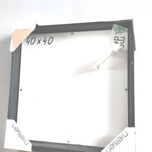 Può includere: Una cornice nera con interno bianco. La cornice misura 40 x 40 cm. La cornice ha angoli protettivi in cartone e il marchio "nielsen" è visibile sugli angoli.