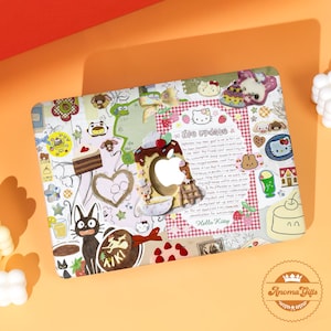 Könnte beinhalten: Eine dekorative Laptop-Hülle mit einem Collage-Design mit Cartoon-Charakteren, Lebensmittelillustrationen und den Texten "life update" und "Hello Kitty". Das Design umfasst einen apfelförmigen Ausschnitt und eine herzförmige Kontur. Das Farbschema ist pastellfarben mit roten Akzenten.