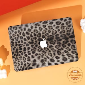 May include: A laptop cover with a leopard print design in shades of gray and black. The Apple logo is visible in the center. The cover is on an orange surface.