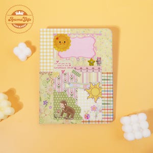 May include: A rectangular notebook featuring a collage of pastel patterns, including yellow gingham, floral prints, and stripes. The cover displays a cartoon sun, a monkey, a star, and the text Let all you do be done in love Corinthians 16:14.
