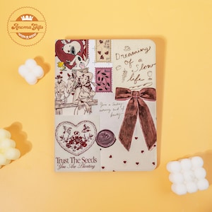 May include: A decorative notebook with a collage design. The cover features illustrations of Snoopy, a woman with horses, stamps, a bow, and hearts. Text includes "Dreaming of a Slow Life" and "Trust The Seeds You Are Planting."