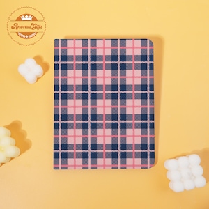 May include: A notebook with a pink and navy blue plaid pattern. The notebook is rectangular with rounded corners. The background is a solid yellow color. The notebook has the text "Aroma Gifts" in a circular logo.