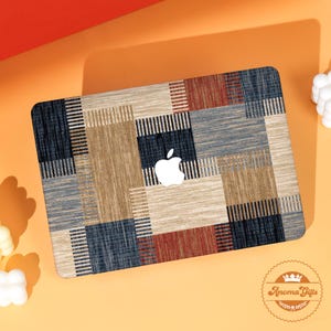 May include: A laptop skin with a geometric pattern in beige, navy, and red. The design features a patchwork of rectangles and squares. The Apple logo is visible. The skin is a decorative accessory for a laptop.