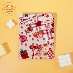 May include: A rectangular notebook with a strawberry shortcake theme. The cover features a pink background with strawberries, a red bow, and the text "Strawberry Shortcake". A red and white checkered pattern is also present.