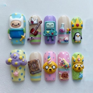 May include: A set of ten artificial nails, each adorned with colorful, cartoon-themed designs. The nails feature characters and objects from the animated series, including Finn, BMO, Jake the Dog, and other whimsical elements. The nails are painted in various colors.