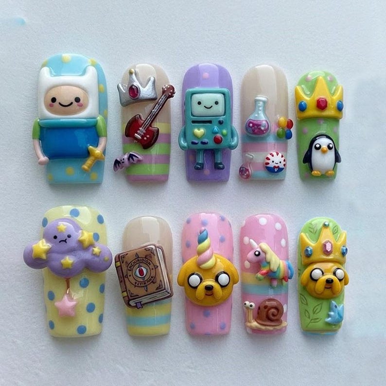 May include: A set of ten artificial nails, each adorned with colorful, cartoon-themed designs. The nails feature characters and objects from the animated series, including Finn, BMO, Jake the Dog, and other whimsical elements. The nails are painted in various colors.
