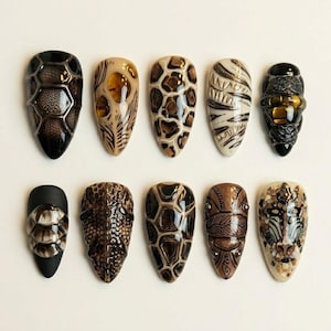 Könnte beinhalten: Zehn mandelförmige Kunstnägel mit detaillierten Designs. Die Nägel zeigen Muster wie Reptilienhaut, geometrische Formen und abstrakte Kunst in Braun, Schwarz und Beige. Jeder Nagel hat ein einzigartiges Design und zeigt aufwendige Kunstfertigkeit.