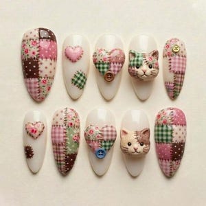 May include: A set of ten almond-shaped press-on nails featuring a patchwork design with floral, polka dot, and gingham patterns in pink, green, and brown. Embellishments include three-dimensional cat faces, hearts, and small buttons.