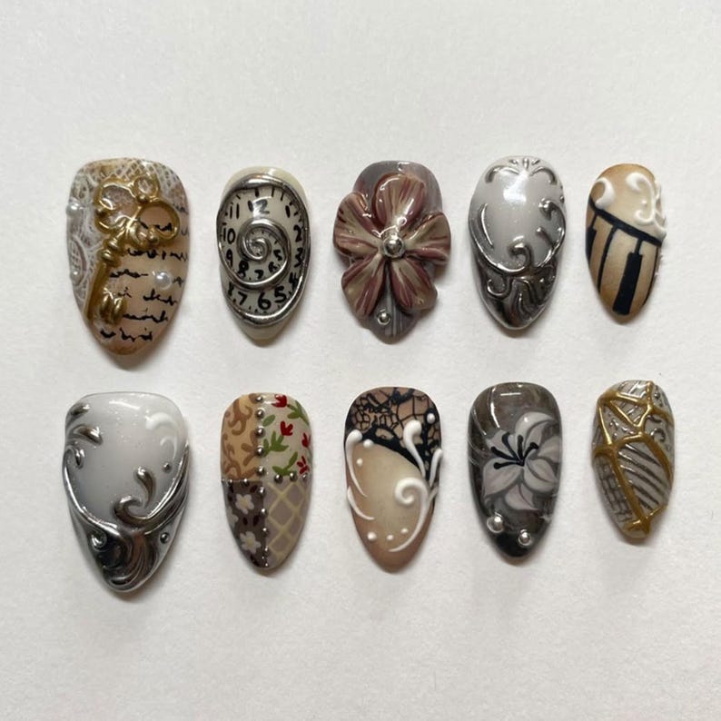 Puede incluir: Un conjunto de diez u&ntilde;as artificiales con varios dise&ntilde;os. Las u&ntilde;as presentan patrones intrincados, incluyendo motivos florales, de reloj y abstractos. Los colores incluyen beige, marr&oacute;n, gris y dorado, con detalles plateados. Cada u&ntilde;a tiene un dise&ntilde;o &uacute;nico.
