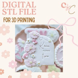 Può includere: File STL digitale per la stampa 3D. Un biscotto rosa chiaro decorato con fiori rosa e bianchi. Il biscotto è inciso con "Kavia turns two". Lo sfondo è rosa chiaro con illustrazioni floreali.