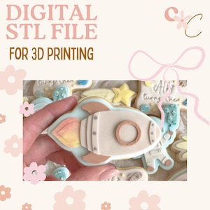 Può includere: Una collezione di biscotti di zucchero decorati, tra cui un razzo, una stella e un astronauta. Il biscotto a forma di razzo è bianco sporco con un contorno azzurro e fiammate arancioni e gialle. Il testo "DIGITAL STL FILE FOR 3D PRINTING" è in alto.