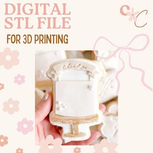 May include: A digital STL file for 3D printing. The image shows a decorated cookie in the shape of a cake. The cookie is white with gold accents and has the word "thirty" written on a banner. The background is a soft pink with floral and bow graphics.