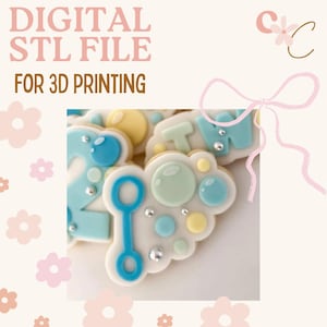 Puede incluir: Archivo STL digital para impresión 3D. La imagen presenta galletas decoradas con glaseado azul, amarillo y blanco. Las galletas tienen forma de burbujas, el número 2 y las letras "TW". El fondo es de color rosa claro con motivos florales.