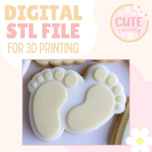 Könnte beinhalten: Ein weißer Keks mit gelber Zuckerguss-Verzierung in Form von zwei Babyfüßen. Der Keks ist mit kleinen gelben Kreisen verziert, die die Zehen darstellen. Der Text "Cute + Crumbly" ist im Hintergrund sichtbar.