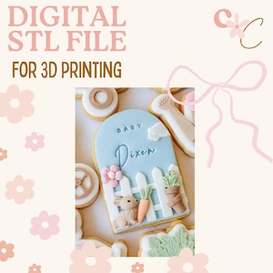 May include: A light blue cookie with the name "Dixon" and the word "Baby" written on it. The cookie is decorated with a bunny, carrots, and a white picket fence. The text "DIGITAL STL FILE FOR 3D PRINTING" is at the top.