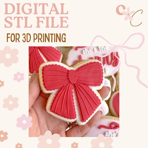 May include: A close-up of a decorated cookie shaped like a bow. The bow is red with white icing around the edges. The text "DIGITAL STL FILE FOR 3D PRINTING" is at the top of the image.