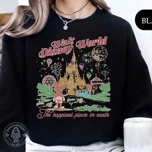 Puede incluir: Sudadera negra con un gr&aacute;fico colorido de Walt Disney World, que incluye un castillo, fuegos artificiales y globos. El texto "Walt Disney World" y "The happiest place in earth" est&aacute; en una fuente retro.