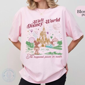 Puede incluir: Camiseta rosa claro con un dise&ntilde;o de Walt Disney World, con un castillo, Mickey Mouse y globos. El texto dice "Walt Disney World" y "The happiest place in earth."