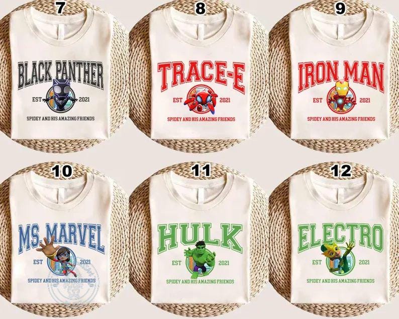 May include: Off-white t-shirts with various superhero designs. Each shirt features a different character name in bold lettering, along with a graphic and the text "Spidey and His Amazing Friends". Characters include Black Panther, Trace-E, Iron Man, Ms. Marvel, Hulk, and Electro.
